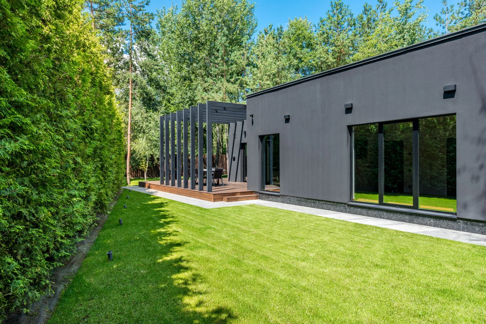Grüner Garten mit gepflegtem Rasen, hoher Hecke und Holzterrasse
